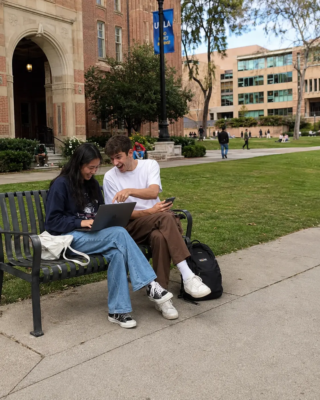 Two friends laughing at a laptop on a park bench